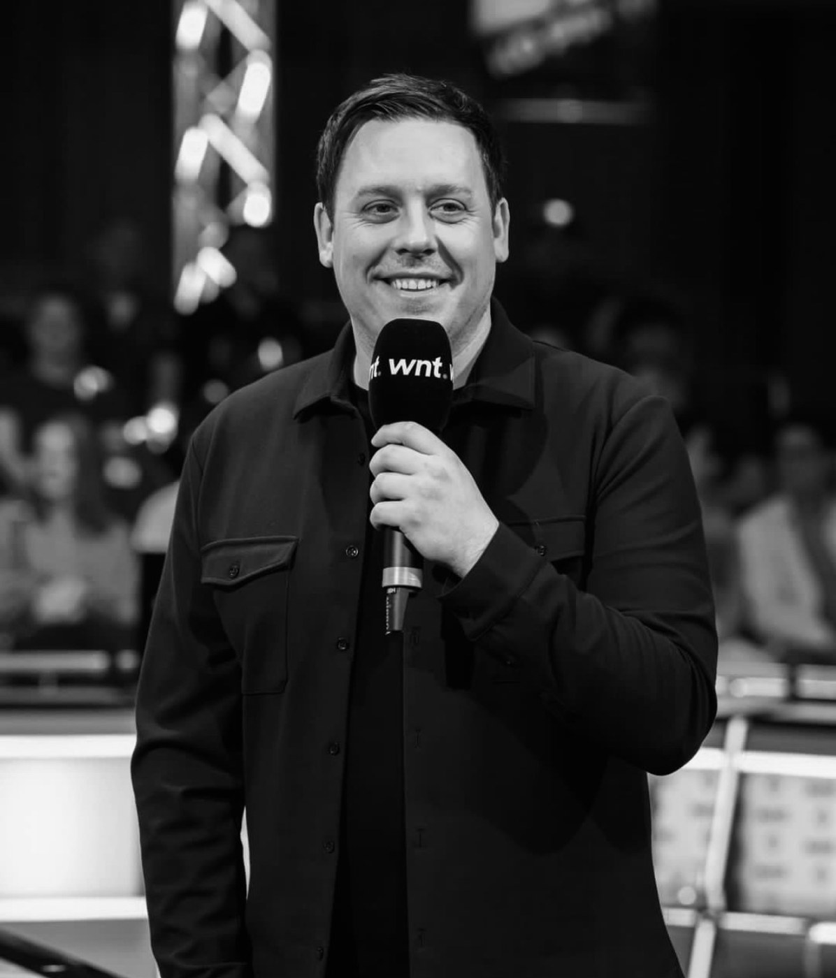 Karl Boyes smiling and holding a microphone beside a pool table